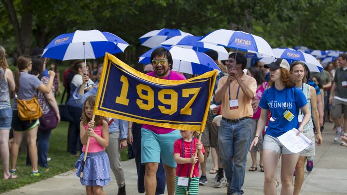 A group of alumni carrying blue and white umbrellas and a banner reading "1997"