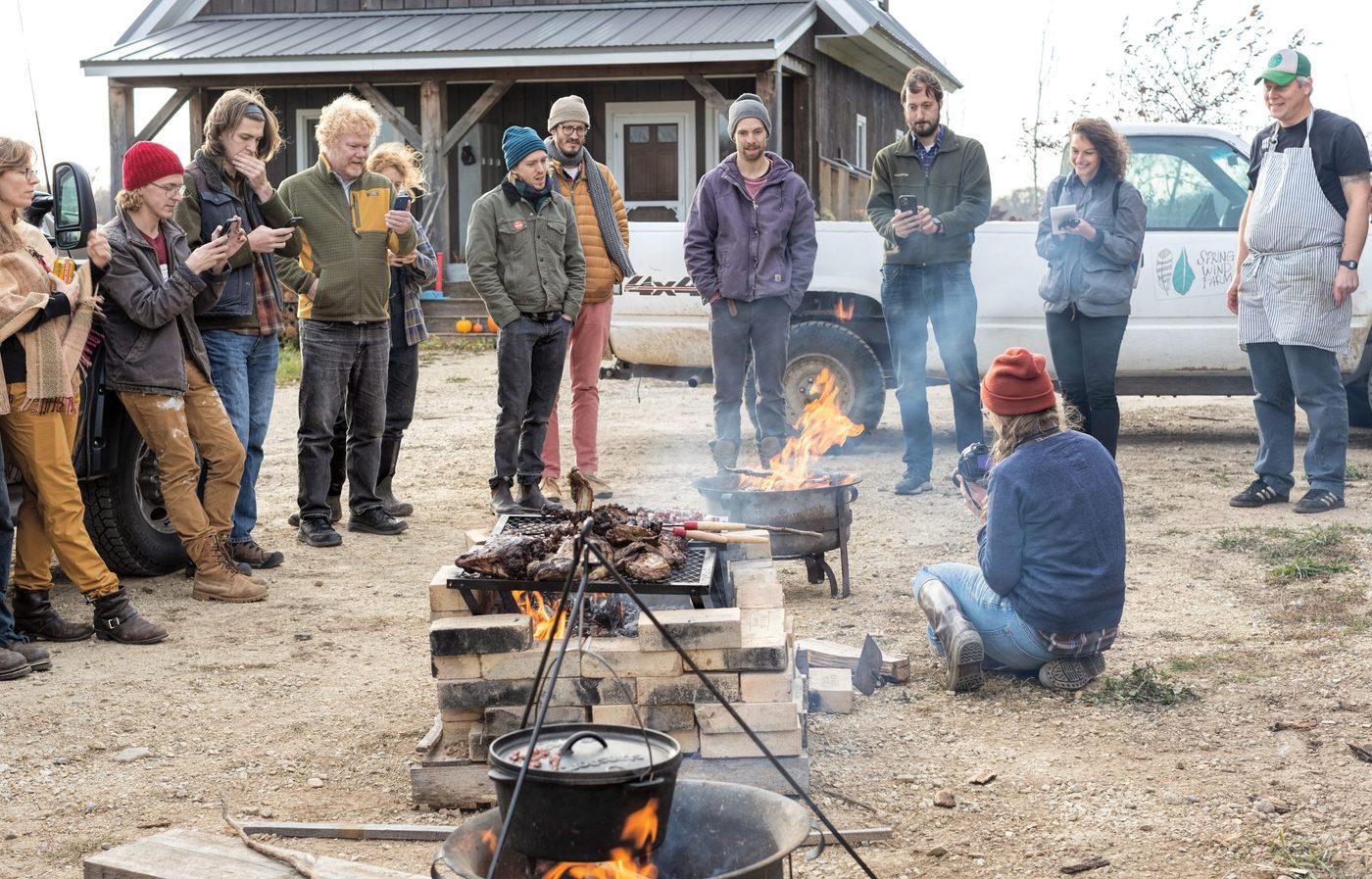 A group of people stand around an outdoor fire as a lamb is cooked in a recreation of an ancient Greek ceremony