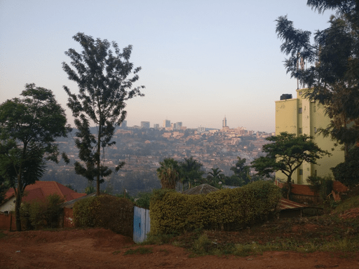 Soft lighting over roofs of houses looking down a hill, with a red dirt road in front.