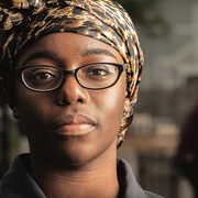 A young Black woman wears an African-print head scarf and looks directly into the camera