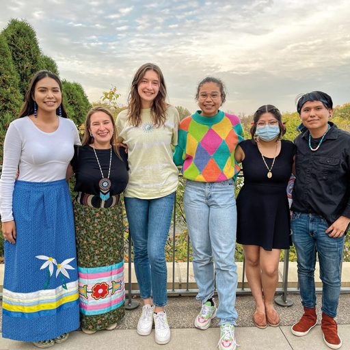 Six people pose for a photo, some wear clothing with traditional native American designs