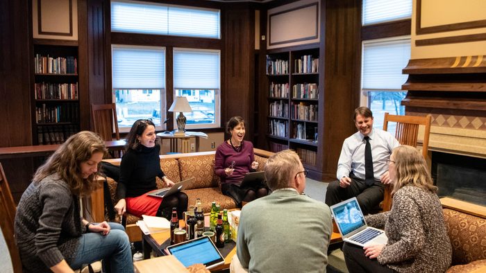 Faculty sit around a table in a book-filled room