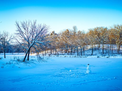 A frozen lake is covered with snow. In the middle of the lake, someone has built a snowman and put a hat on its head.