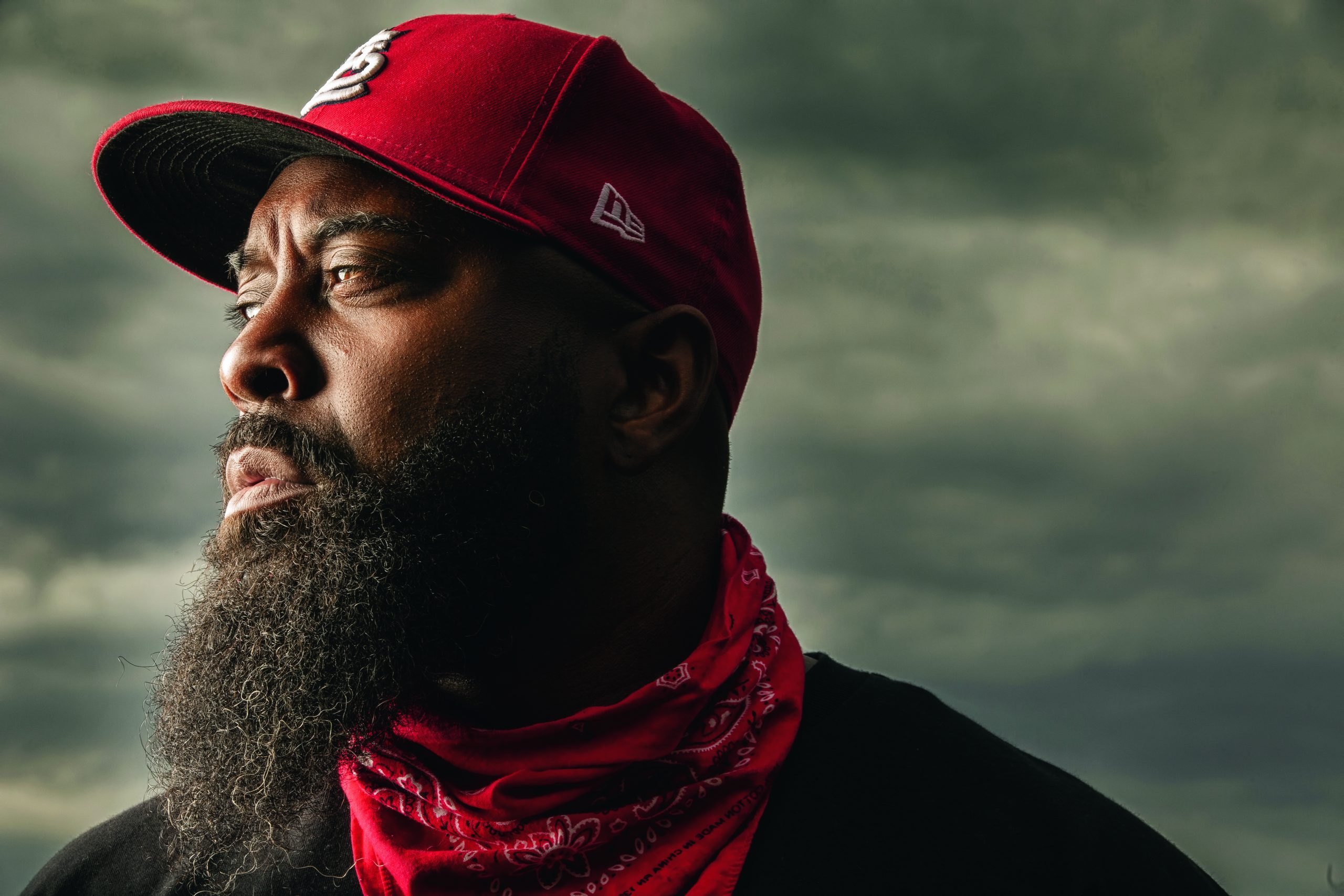 a Black man with a beard wearing a red baseball cap and a red bandana around his neck
