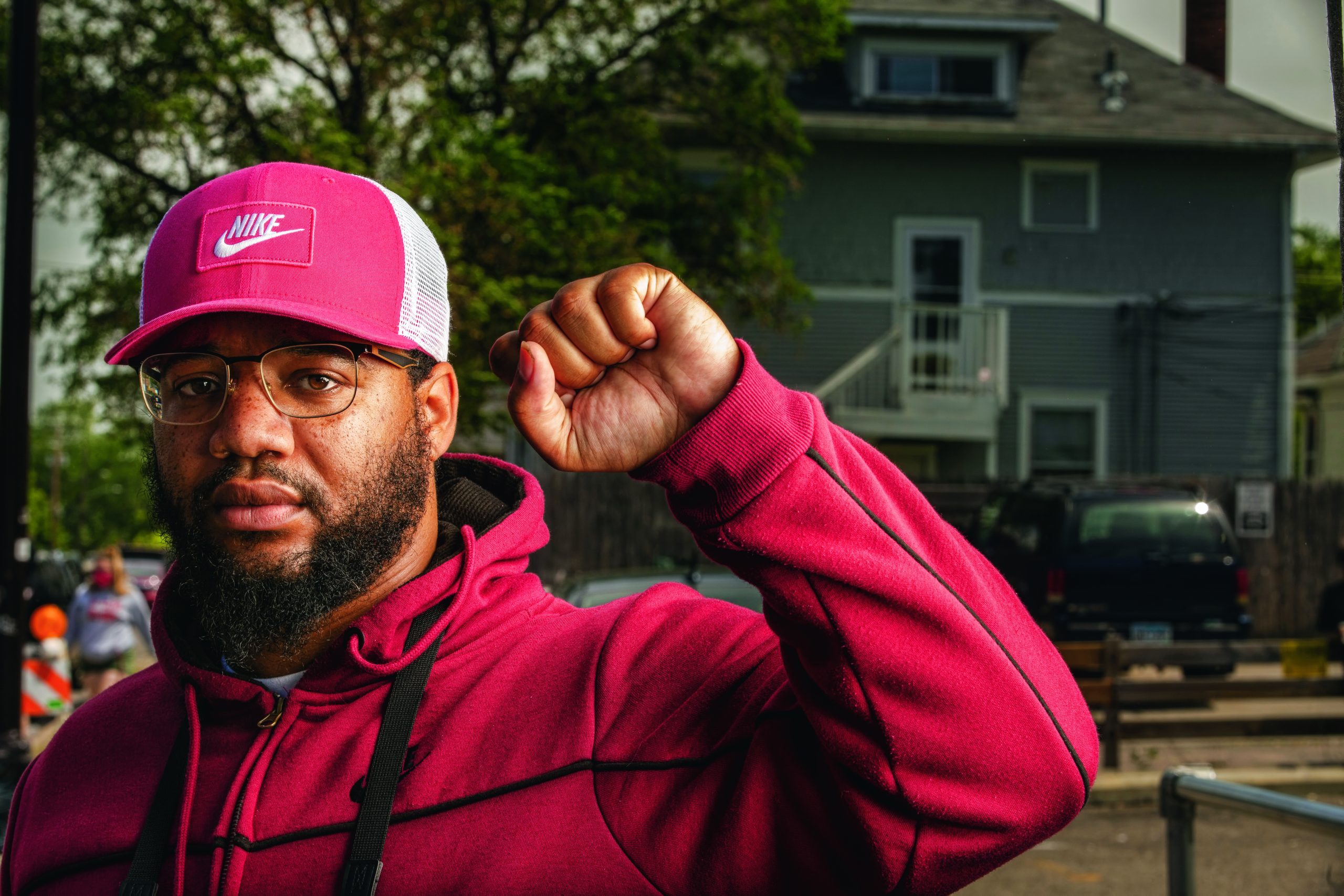 A Black man in a pink tracksuit and pink Nike cap raises his fist