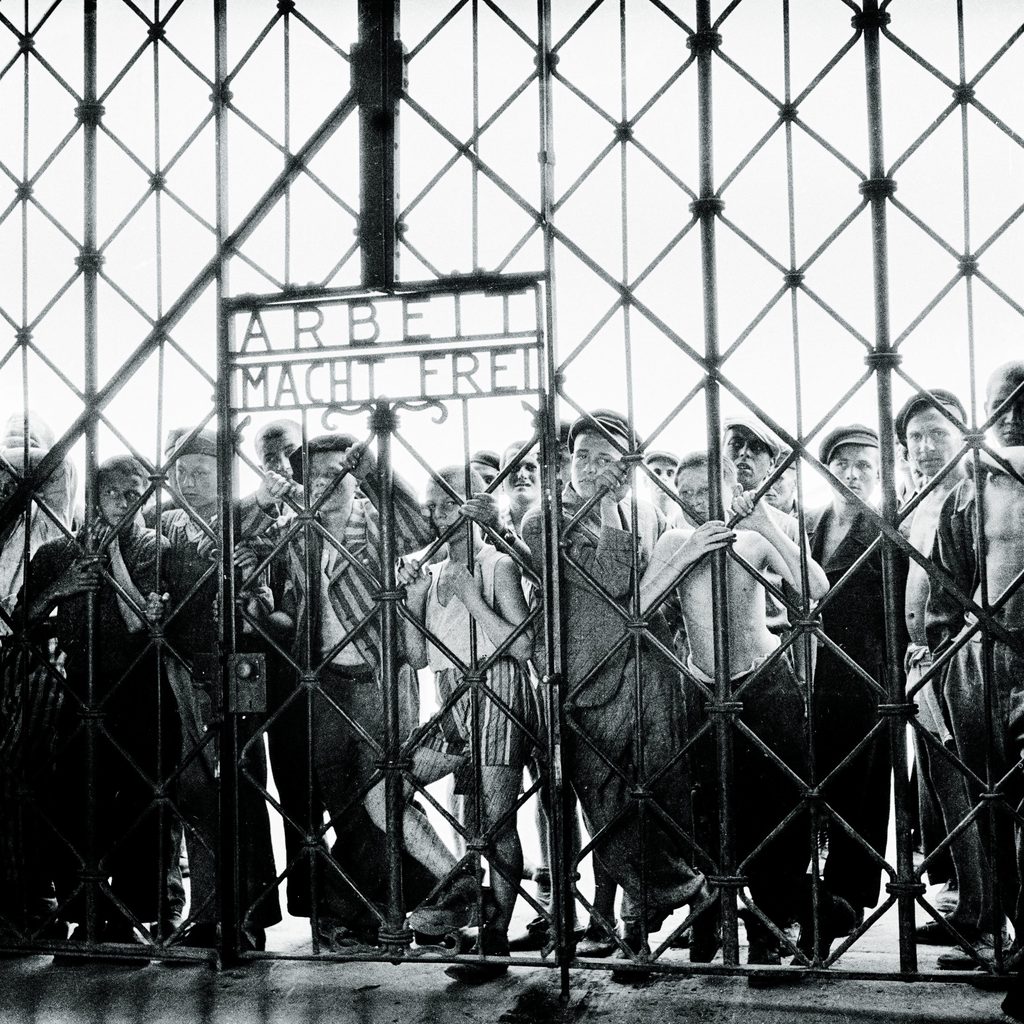 Prisoners in a concentration camp stand behind an iron fence