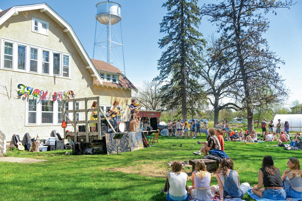 A crowd of people watch a live band on a sunny day at Carleton's Farm House