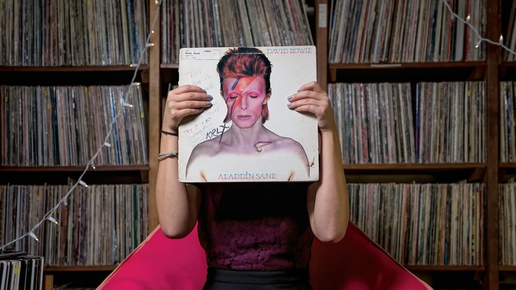 A person holds a record album (David Bowie's "Aladdin Sane") so that the cover photo aligns with their own face
