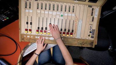Overhead view of a person's hands on the faders of a sound mixer