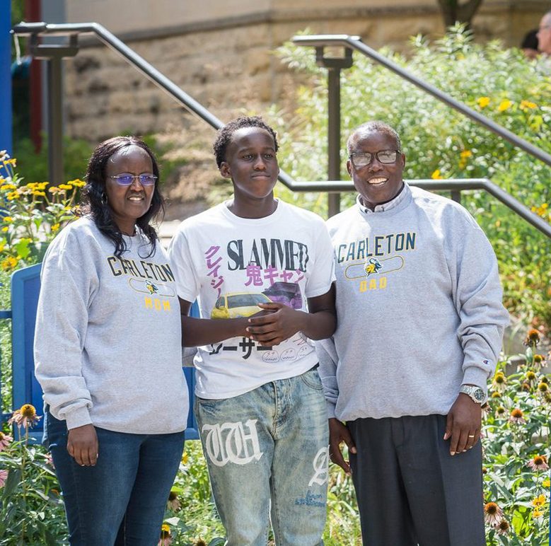 Student standing outside with parents, who are wearing "Carleton Mom" and "Carleton Dad" sweatshirts