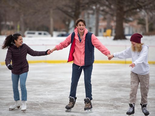 Three students hold hands while skating on the campus ice rink