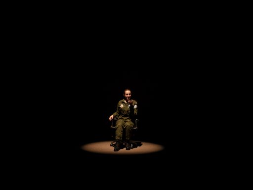 A pilot seated in a chair under a spotlight