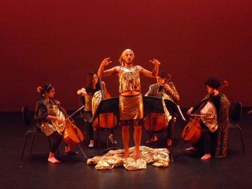 A dancer wearing gold standing in the middle of four cellists