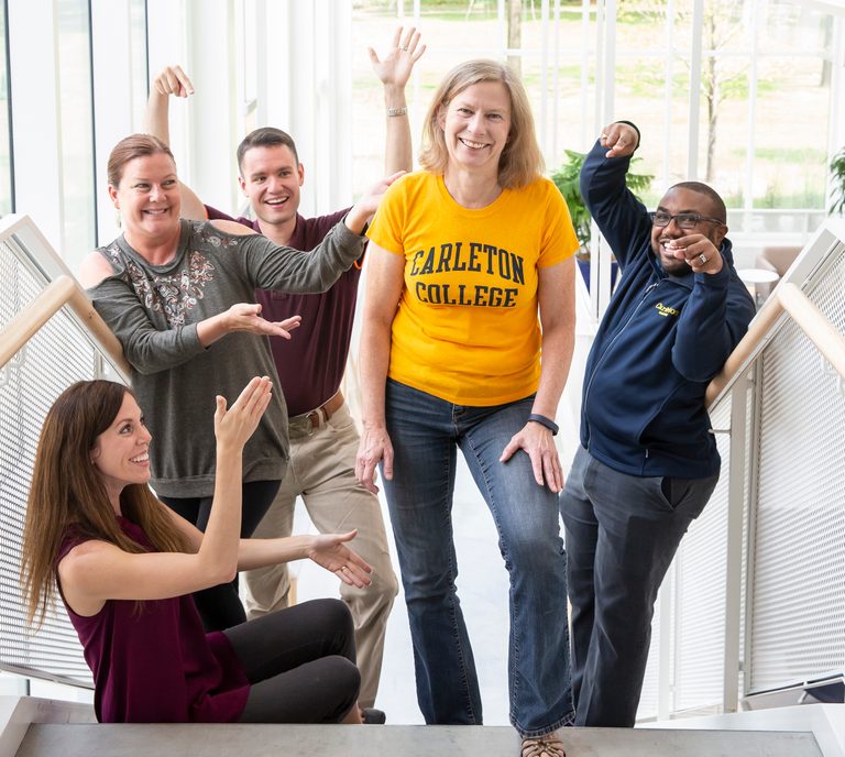 Karen Schilling stands on a stairway surrounded by four Carleton staff members