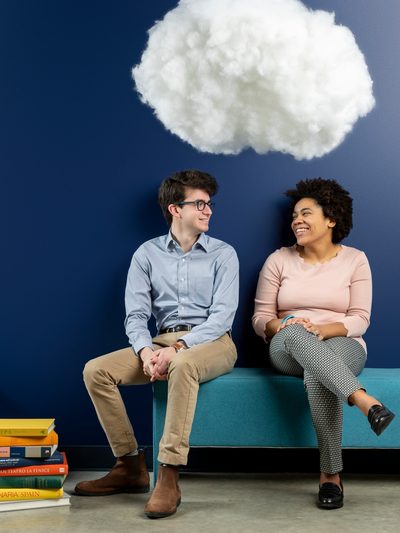 Two smiling students sit on a couch beneath a cotton cloud