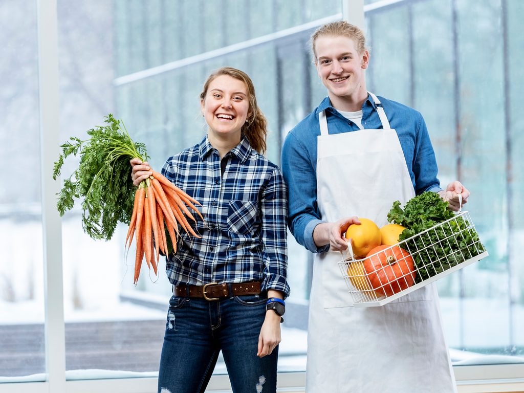Two students smile and pose with an assortment of fresh vegetables