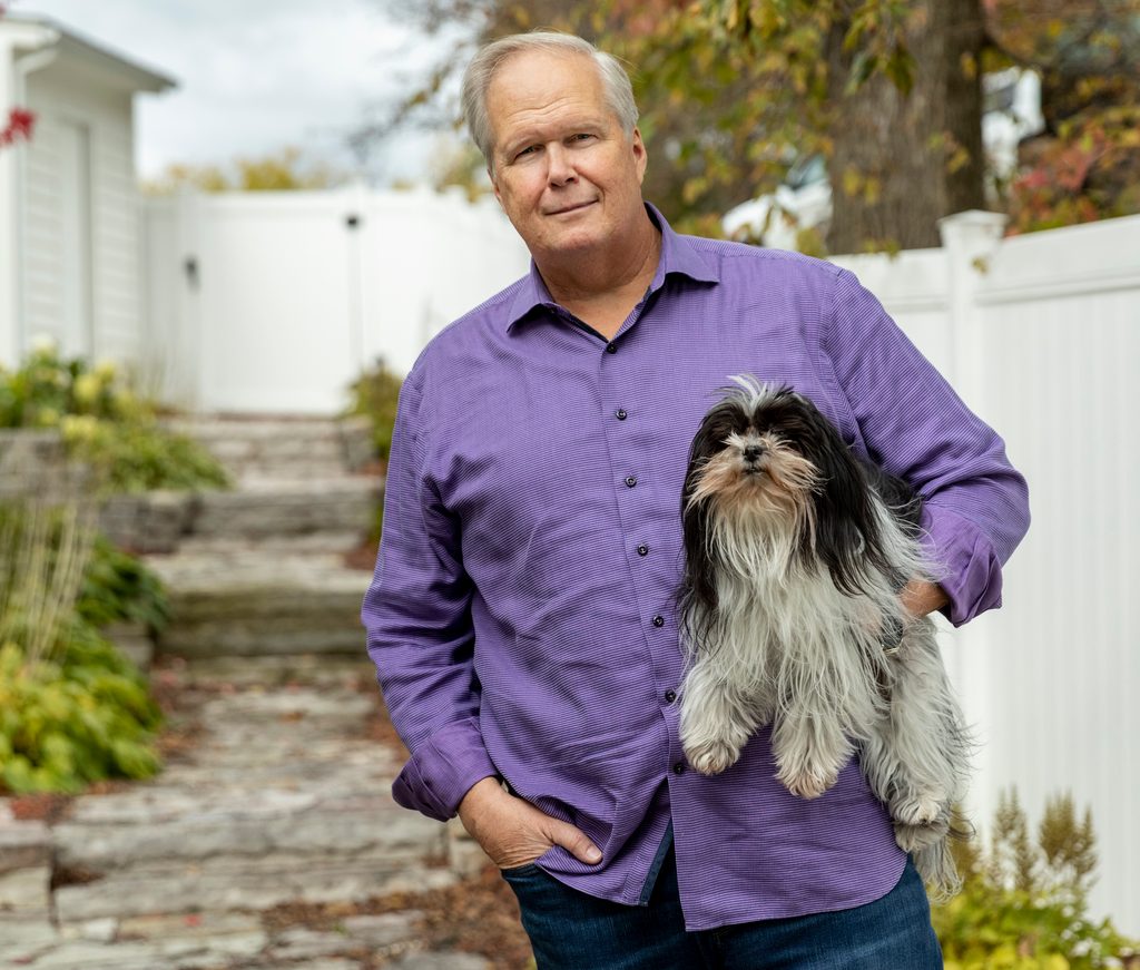 A man poses with a dog under his arm